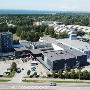 Aerial view of a modern hotel complex with colorful walls, parking lots, trees, and the sea in the distance.