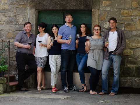 Group of seven adults posing with wine glasses outside a stone building, smiling in front of a green door.