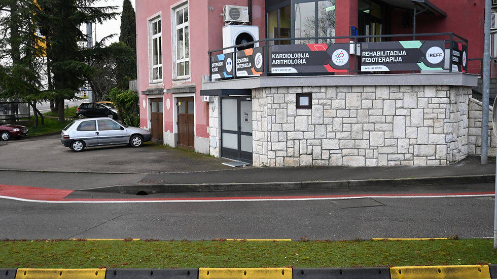 Pink clinic building with signs for cardiology, arrhythmology and rehabilitation; parked car beside a quiet street.