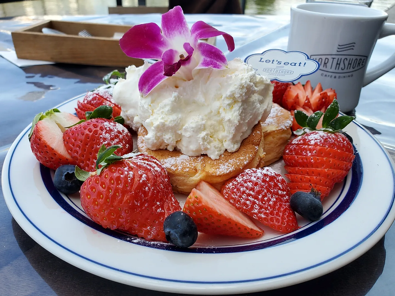 Berry berry pancakes. Pancakes topped with whipped cream in centre of plate, surrounded by berries. Side on photo. Northshore Kitahama, Osaka Japan.