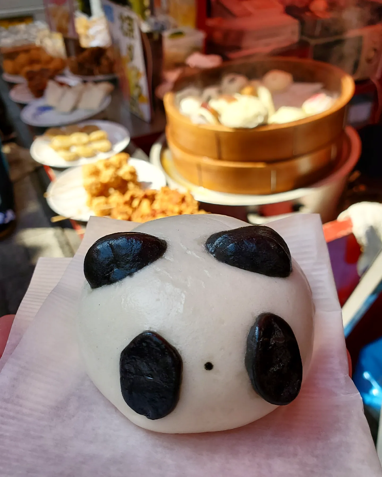 Steamed panda bun filled with sweet black sesame paste with street food in background. Nankinmachi, Kobe Japan.