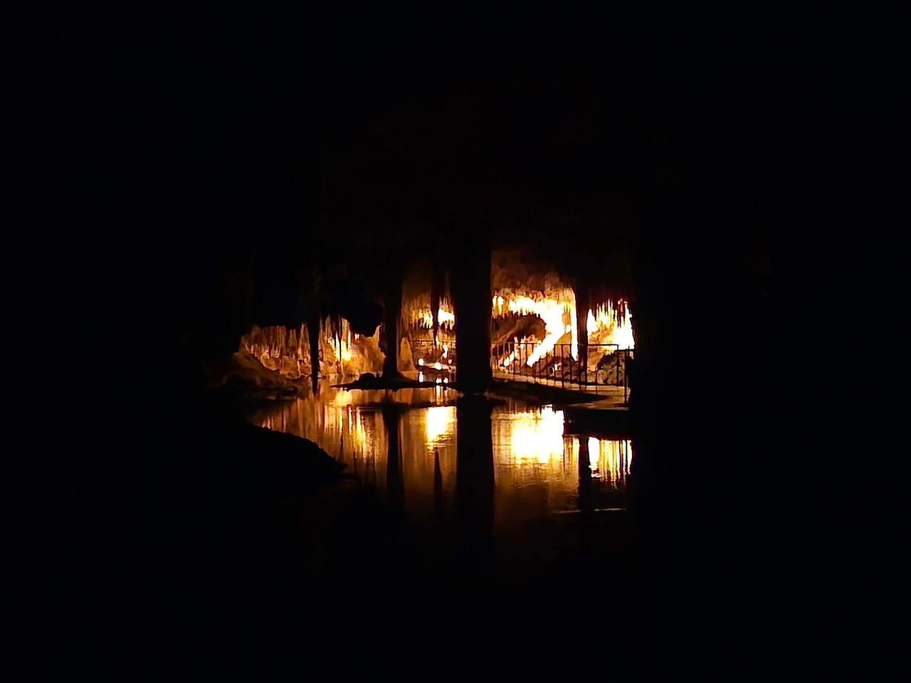 Photo inside Lake Cave (Western Australia). The outside of the photo is black, and the middle of the photo shows a lit-up "suspended table-top" in the distance.