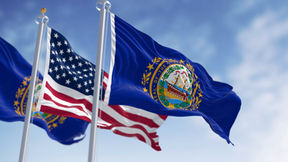 An image of three flags floating in the breeze. The outer 2 are the NH state flag and the inner flag is the US flag.