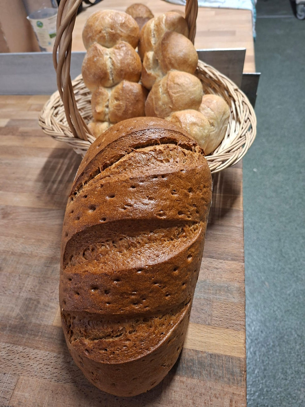 Dunkles Bauernbrot vor einem Korb mit hellen Brötchen