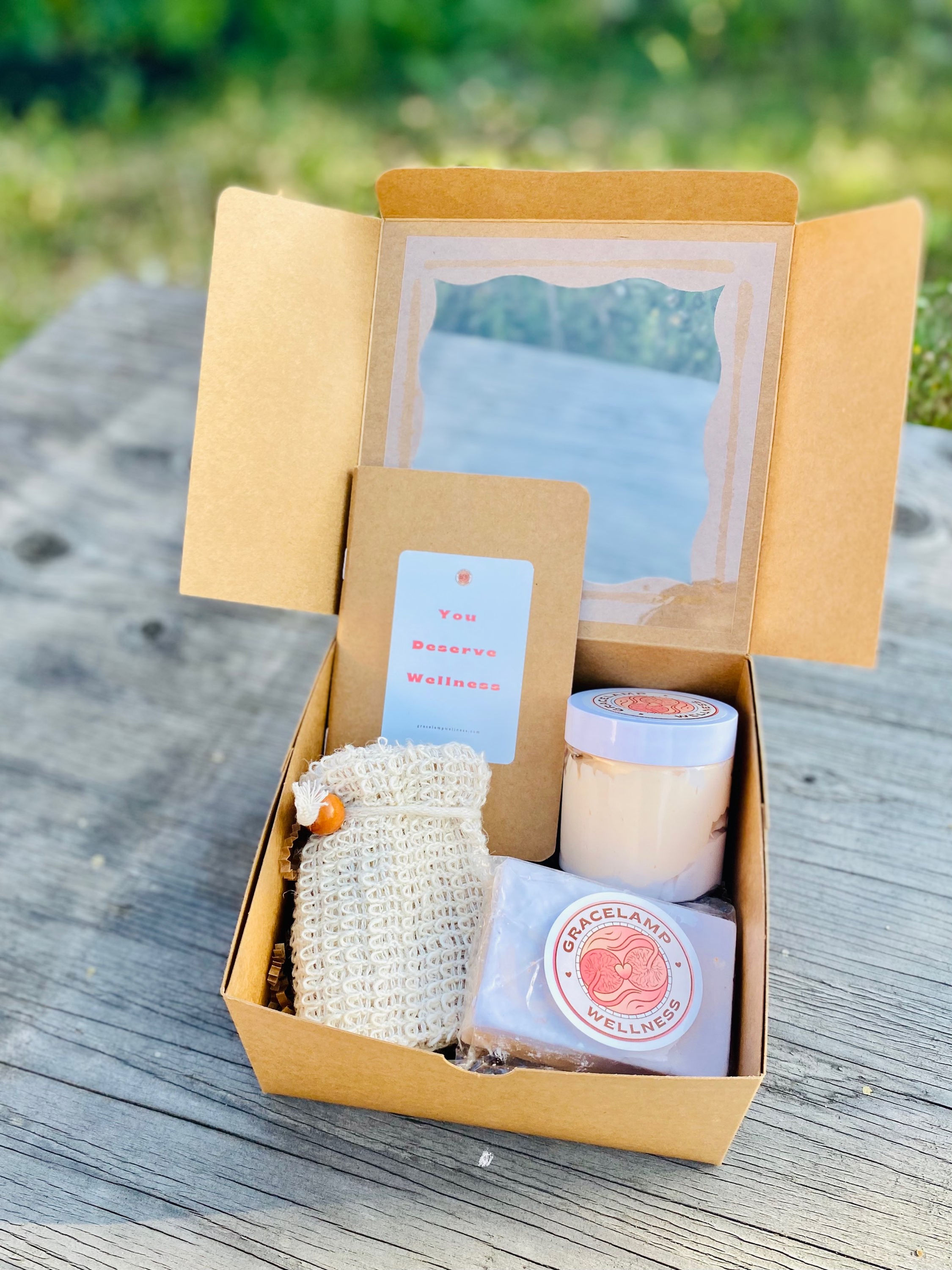 Passionfruit Peach Wellness Gift Box open on top a rustic grey table with orange and purple colored body butter and soap, cream soap scrubber/ holder, and beige "You Are Enough" journal.