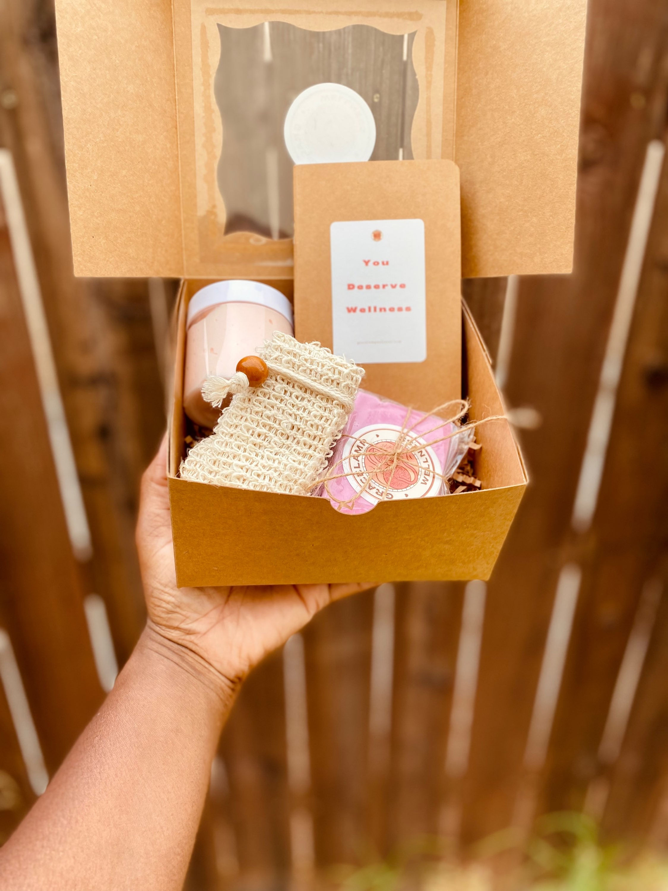 Strawberry Shortcake Gift Box opened with pink body butter, pink soap, beige journal, and cream soap holder, fence background