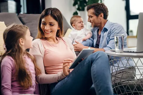 happy-mother-mother-talking-while-surfing-net-touchpad-while-father-baby-boy-are-backgroun