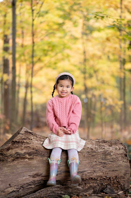 Portrait of a young girl sitting on a tree log during a fall photography session in Hamilton, captured by Liban Creative Studio