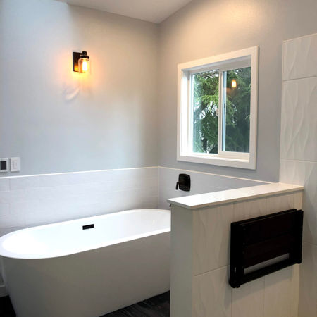 Bright bathroom with a stylish freestanding tub, modern bronze fixtures, and textured tiles, creating an inviting atmosphere.