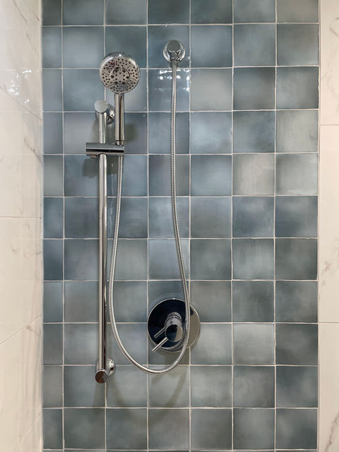 A modern showerhead and faucet mounted on stylish aqua tiled wall, featuring sleek chrome accents and a flexible handheld shower.