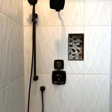 Modern bronze shower fixtures with a hand shower, set against textured white tiles.