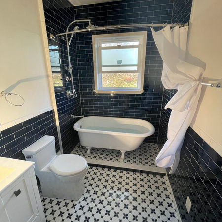 Elegant bathroom remodel with a clawfoot tub, blue subway tiles, and a bold blue-and-white tile floor in a vintage style.