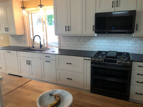 Modern kitchen featuring white cabinetry, black appliances, a dark countertop, and pendant lighting over a sink and workspace.