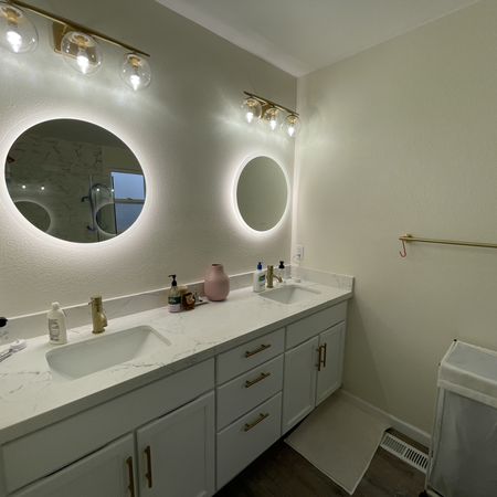 A contemporary bathroom with two back-lit round mirrors above dual undermount sinks, creating a balanced and elegant look.