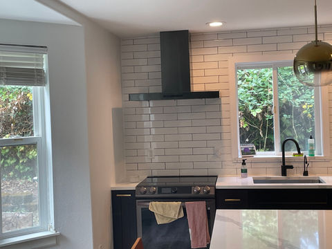 Modern kitchen featuring a stainless steel range, black cabinets, white subway tile backsplash, and a quartz countertop with a window view.