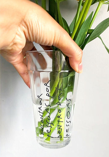 Copo de vidro com flores verdes e frase escrita à mão: 'Encontrar pessoas por dentro das pessoas