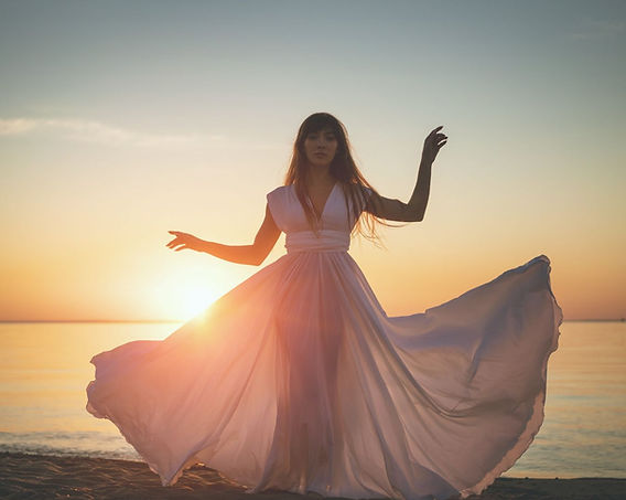 Woman on a beach standing in front of a pink and blue sky as the sunrises