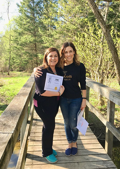 Martha Eleftheriou with Rosie, a past Reiki student. They are standing on a bridge with beautiful green trees behind them