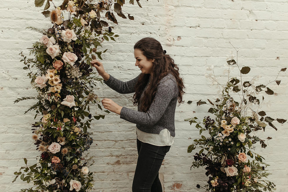 Florist with dark hair creating floral arch arrangement.