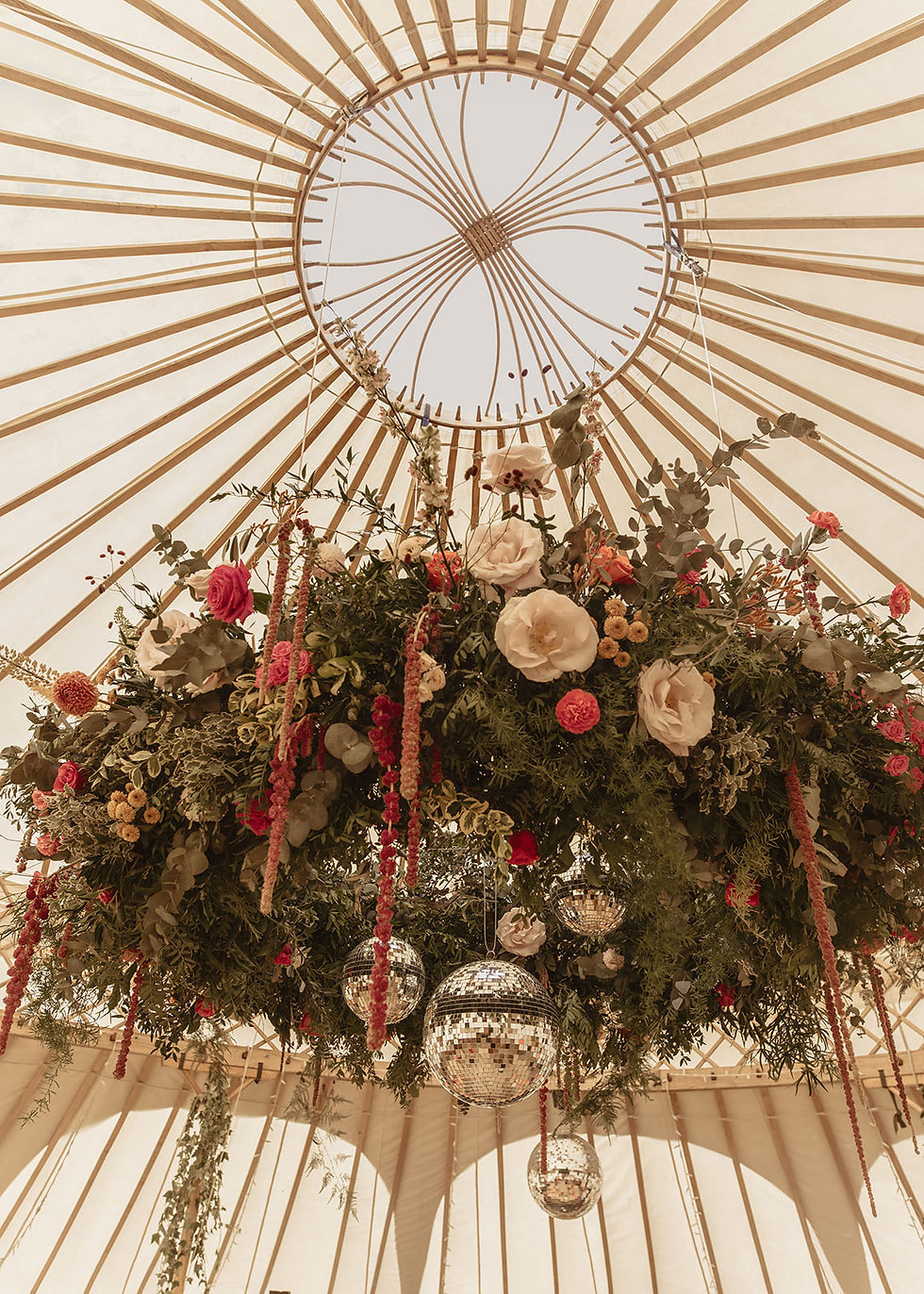 white yurt decorated with a hanging hoop of foliage and pink and orange flowers with disco balls in the center