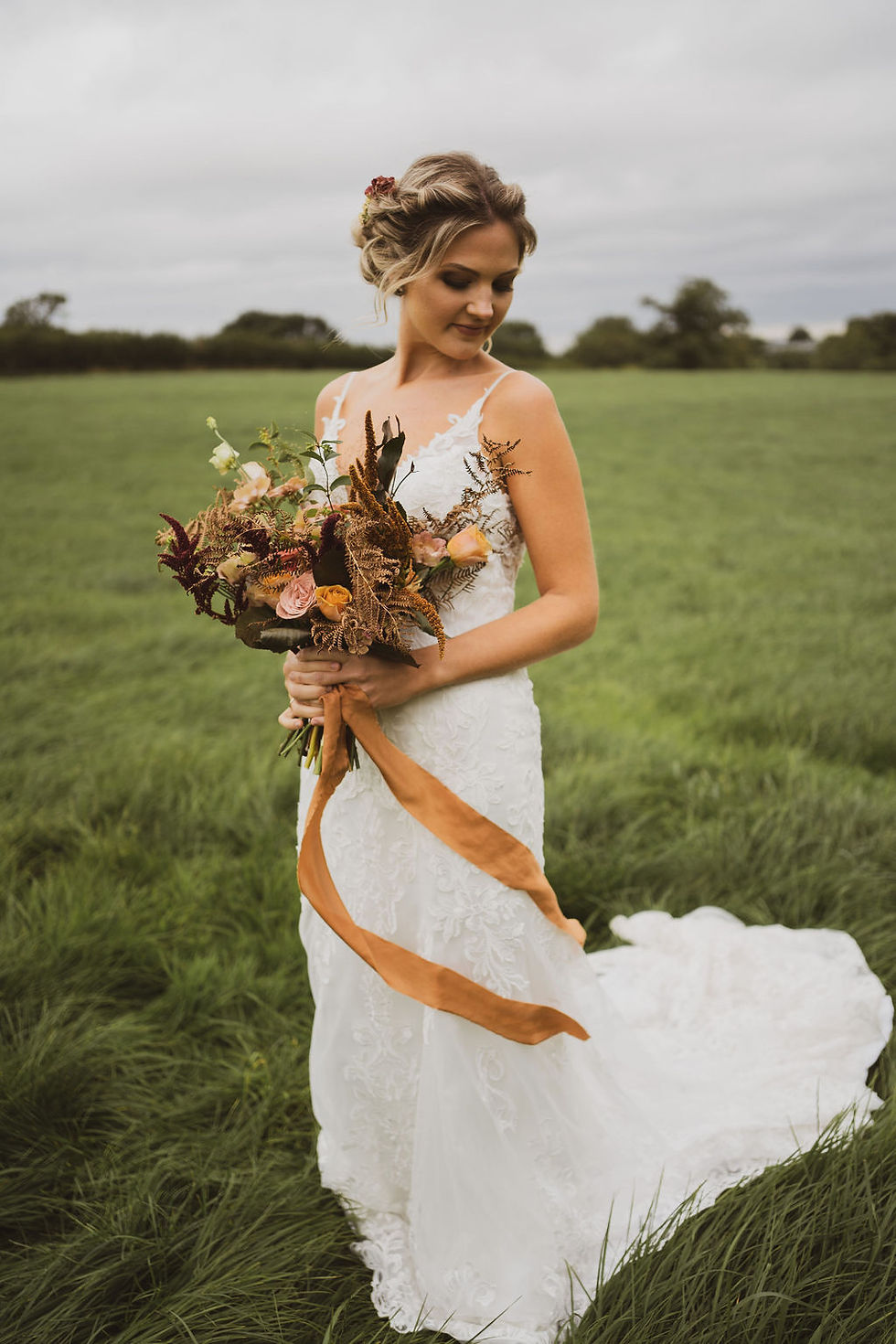 Bride in white wedding dress holding an autumnal fall bridal bouquet with trailing silk ribbons