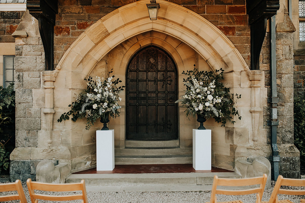 Floral urn arrangements on white plinths in front of arched doorway in period house