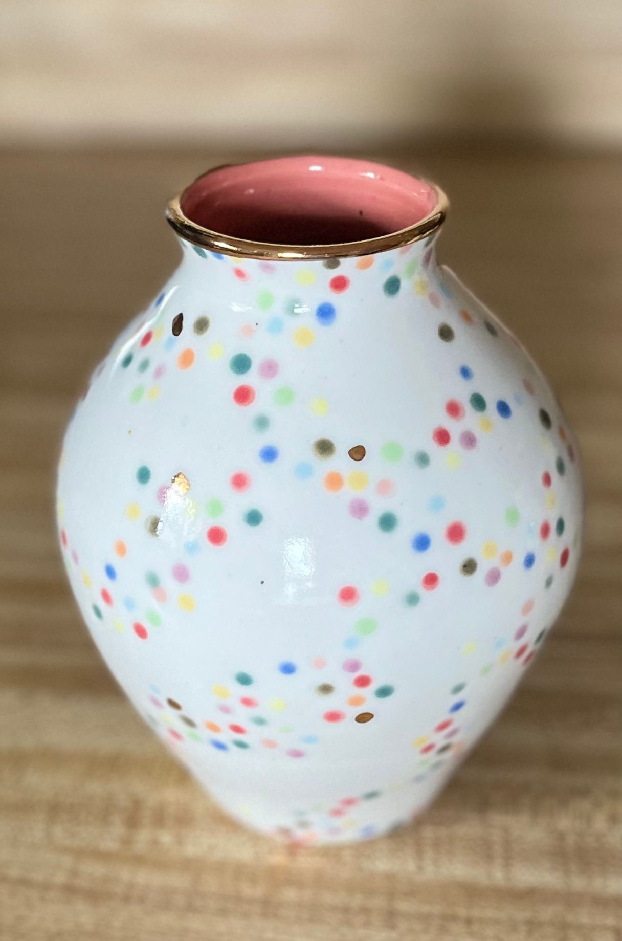 Colorful polka dot porcelain ceramic vase with gold trim and details. Home decor setting front view.