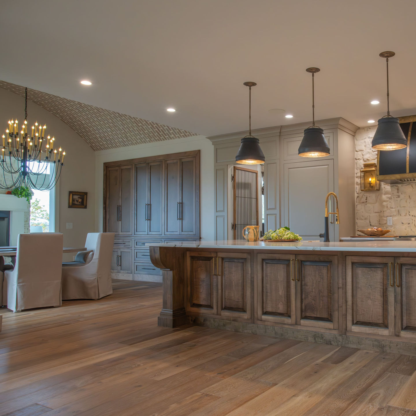 A spacious kitchen featuring warm wood tones, sophisticated pendant lighting, and an inviting dining area with a grand chandelier, blending luxury and comfort.
