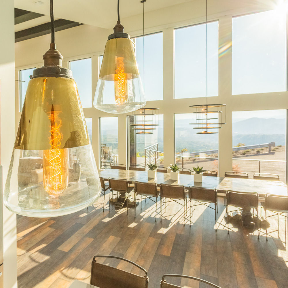 A stunning dining area with floor-to-ceiling windows offering panoramic views, complemented by elegant pendant lighting, a long wooden table, and modern rustic decor.