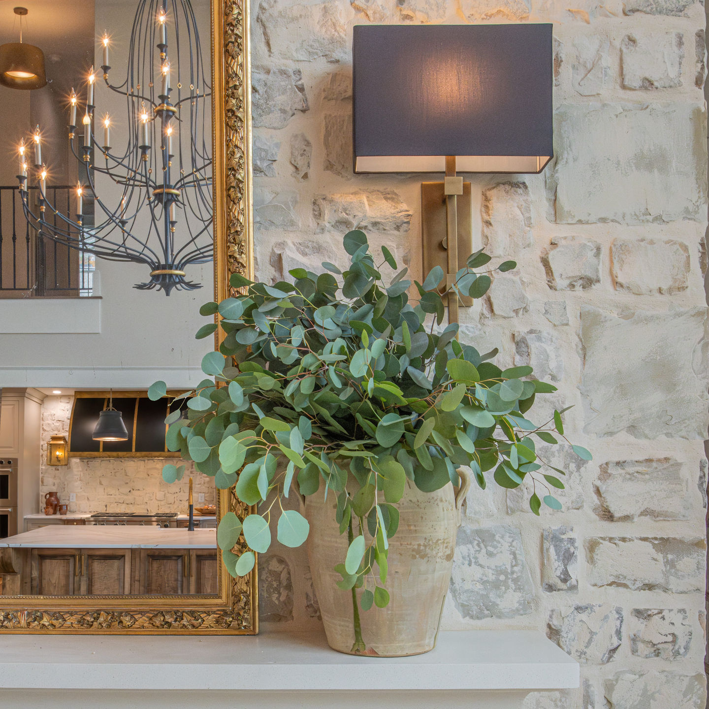 A beautifully styled mantel with a gold-framed mirror, modern wall sconces, and lush greenery, adding charm to a rustic stone fireplace.