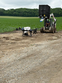 Commercial agricultural drone used for precision crop spraying in a farm field with support equipment nearby