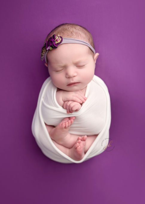 newborn baby girl wrapped in white fabric on magenta background