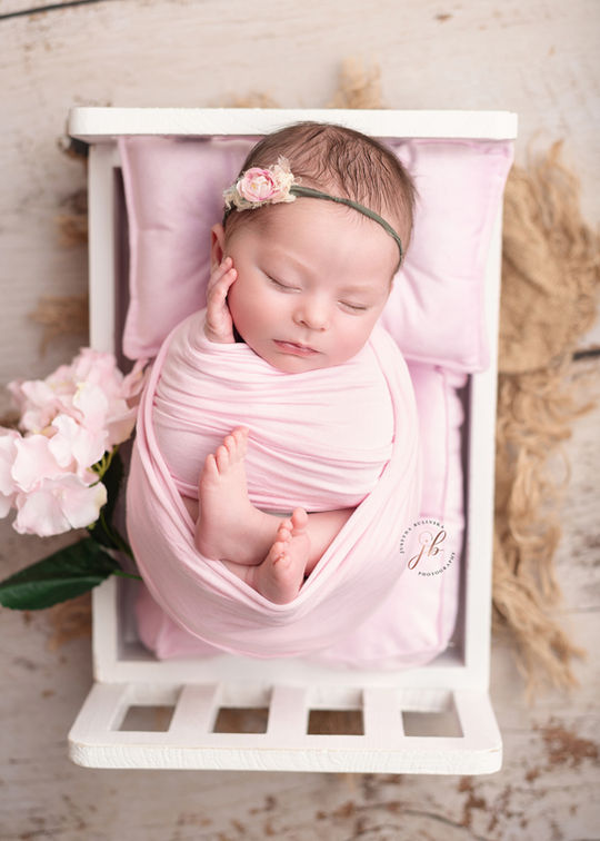 newborn baby girl in pink on white wooden bed