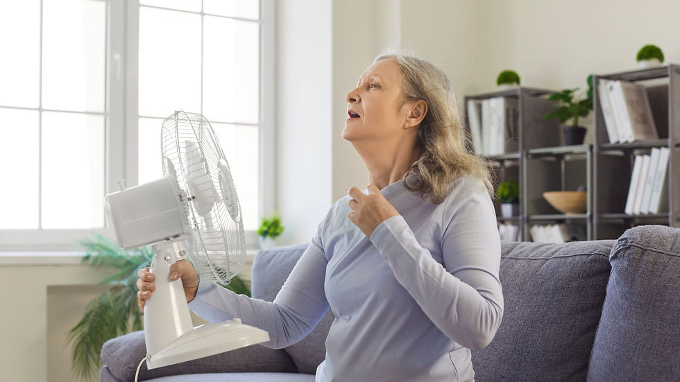 A woman sitting in her living room holding a fan up to her face trying to cool down.