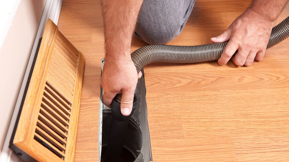 man kneeling down on the floor with a floor vent grate lifted off the vent and a vacuum hose in the duct.
