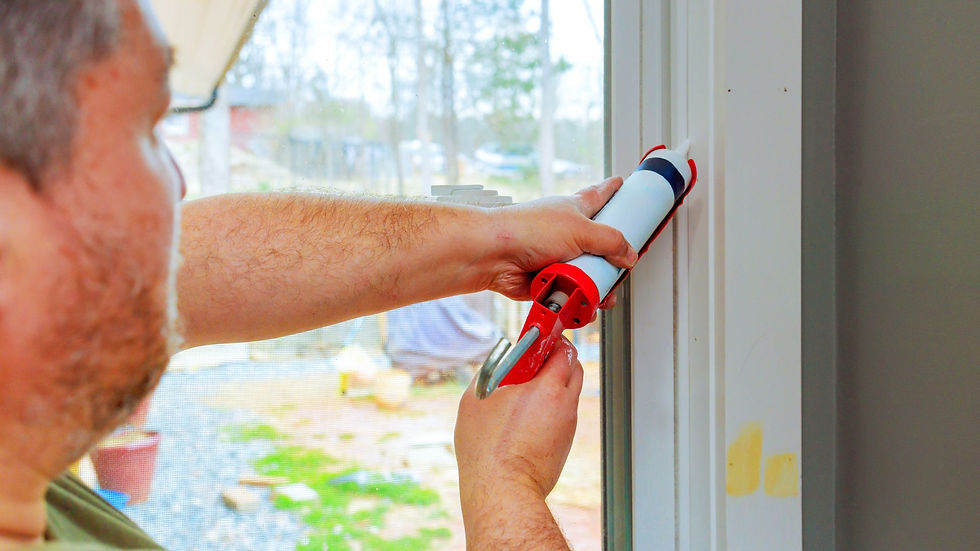 man caulking a window frame with the window open and a yard in the background with a grill that is covered for the season