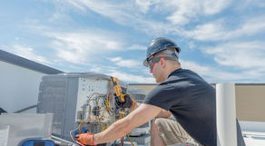 HVAC technician working on a rooftop unit. He has gauges and other tools and is evaluating how the unit is working.