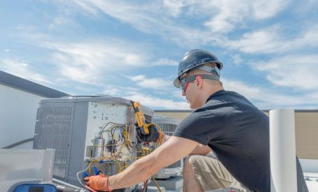 HVAC technician working on a rooftop unit. He has gauges and other tools and is evaluating how the unit is working.