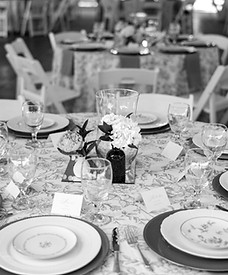 A reception table with floral tablecloths, peony, hydrangea and candle centerpieces. Beautiful plates and flatware on gold chargers.