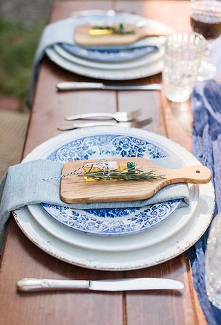 Une assiette témoin d'un mariage avec une petite planche à découper et une petite bouteille d'huile d'olive posée sur une assiette en céramique bleue