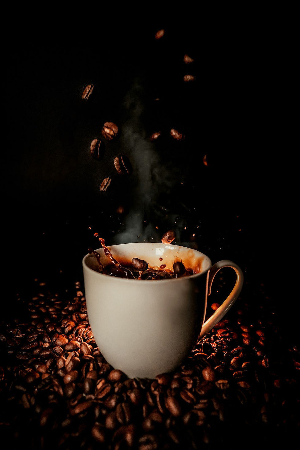 A coffee cup with coffee beans falling into it on dark background