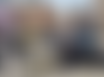 Woman in denim jacket, headphones around neck, sitting on city steps using smartphone. Busy street with traffic, buildings, vibrant signs.