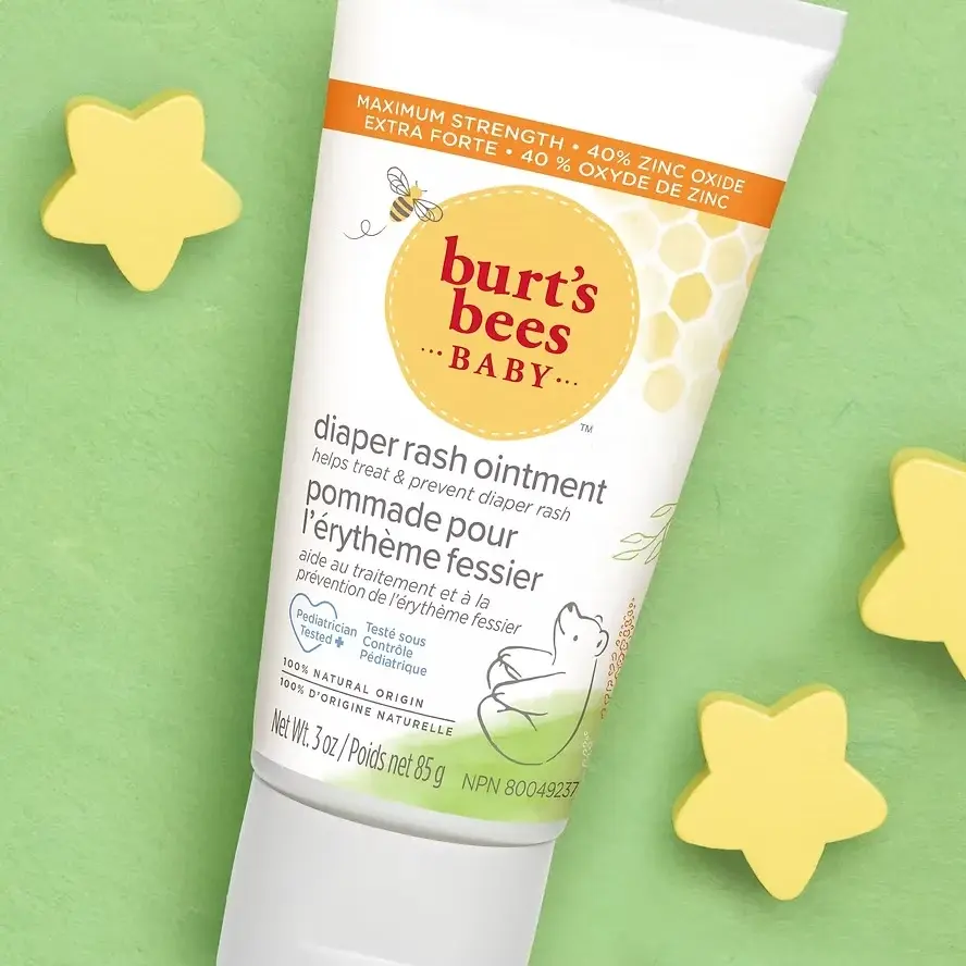 Tube of Burt's Bees Baby diaper rash ointment on green background with yellow star shapes. Text highlights 40% zinc oxide.