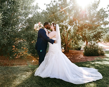 Inerracial couple kisses in golden hour light in front of trees the weddig day