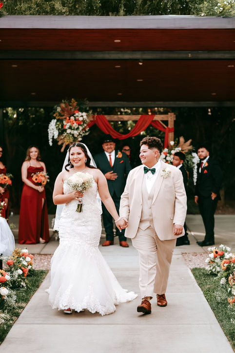 Two brides walking hand in hand down the aisle after their wedding ceremony at Lotus House Las Vegas surrounded by guests and floral arrangements.