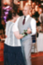 A man in a gray suit and woman in a polka dot dress dance, her wearing a rose corsage. Warm lighting and patterned chairs in the background. Cili at Bali Hai wedding Las Vegas photographer
