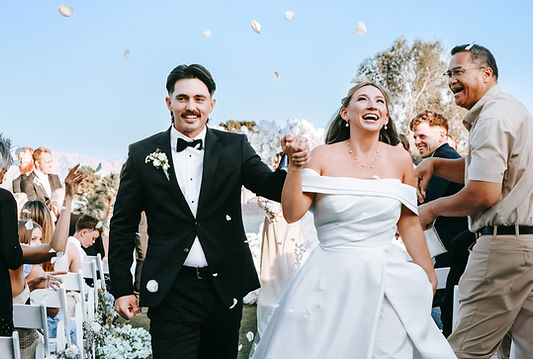 Bride and groom walk down the aisle where everyone is cheering and guests are throwing rose petals