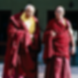 Two elder Tibetan lamas in maroon robes standing outdoors