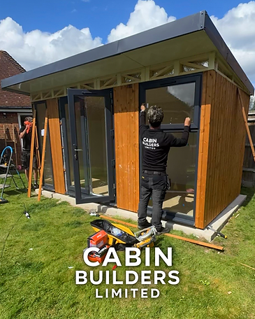 Cabin Builders Limited team fitting glazing to a timber-clad garden office during installation.