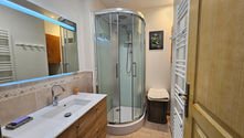 Une salle de bain contemporaine, dotée d’une douche moderne, d’un grand miroir rétro-éclairé et d’un sèche serviette. L’espace respire la propreté et la fonctionnalité, parfait pour un moment de détente après une journée de randonnée ou de ski.
